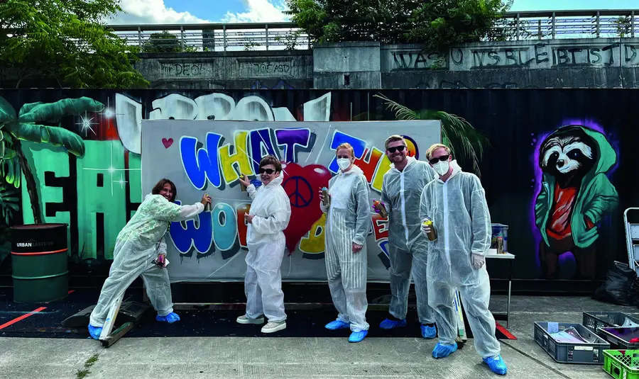 Gruppe in Schutzanzügen vor einer selbst gestalteten Graffitiwand