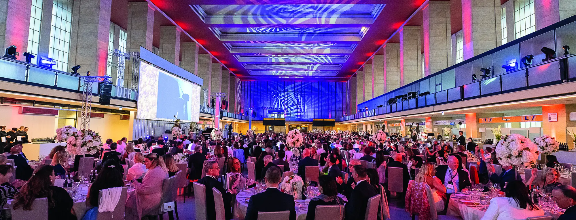 Festlich beleuchtete Halle mit Galatafeln und Bühne